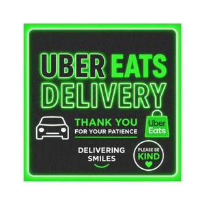May include: Square sign with a black background and a neon green border. The text "UBER EATS DELIVERY" is displayed in large, neon green letters. Additional text includes "THANK YOU FOR YOUR PATIENCE", "DELIVERING SMILES", and "PLEASE BE KIND".