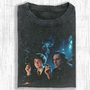 May include: Dark gray t-shirt featuring a graphic of two people smoking cigars. The image has a vintage, distressed look. One person is wearing glasses and a tie. The other person has long dark hair.