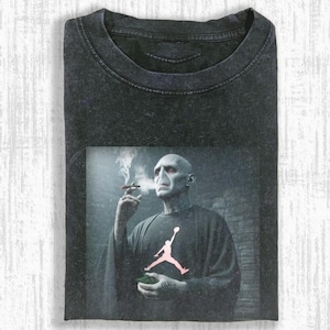 May include: Dark gray t-shirt featuring a graphic of a bald man smoking a cigar, with a pink Jumpman logo on the shirt. The image has a smoky, atmospheric background, and the shirt has a worn, vintage look.
