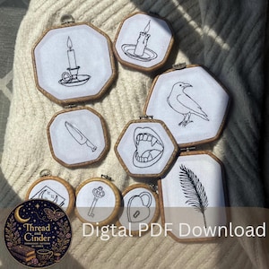 Puede incluir: Una colección de aros de bordado con varios diseños de arte lineal negro sobre tela blanca, incluyendo una vela, un cuervo, un cuchillo y una pluma. Los aros tienen marcos de madera. El texto "Digital PDF Download" es visible.