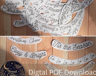 Può includere: Una collezione di strisce di tessuto bianco con frasi natalizie ricamate in nero, tra cui Sleigh, Merry Everything, Tis the Season, Believe, Meet Me, Cozy & Bright e Fa La La. È visibile un logo circolare con il testo Thread and Cinder.