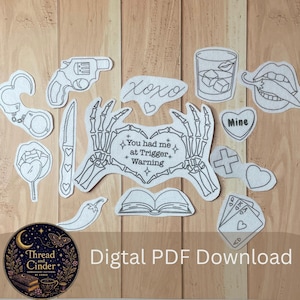 May include: A collection of black and white embroidery pattern cutouts featuring a revolver, handcuffs, a knife, a glass with ice, lips biting a chilli, a heart with the text Mine, a cross, playing cards, and skeleton hands framing the text You had me at Trigger Warning.