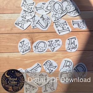 Op de afbeelding: Een verzameling witte stoffen patches met zwarte geborduurde letters, elk versierd met een bloemmotief. De letters vormen woorden zoals LOVE en liggen verspreid. Een cirkelvormig logo met de tekst Thread and Cinder Digital PDF Download is zichtbaar in de linkerbenedenhoek.