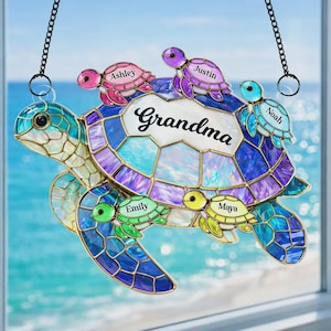 May include: A stained glass turtle suncatcher with the word "Grandma" and the names Ashley, Justin, Noah, Emily, and Maya. The turtle is blue, purple, and teal with a chain for hanging.
