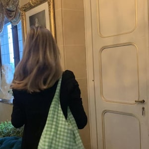 May include: A light green and white gingham patterned hobo bag with a soft, unstructured shape and a wide shoulder strap, worn over a black long-sleeved top and blue denim jeans, showcasing a casual and functional accessory design.