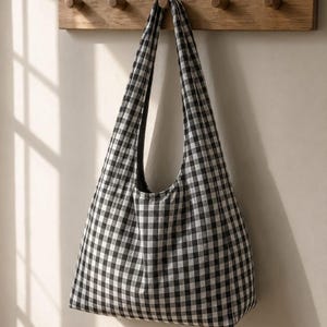 May include: A hobo-style shoulder bag featuring a classic black and white gingham check pattern. The bag has a single integrated shoulder strap and a soft, unstructured silhouette, constructed from a woven fabric with a consistent grid design.