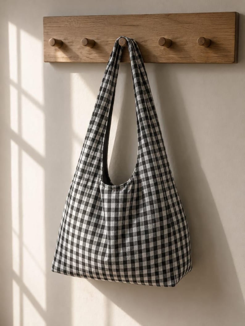 May include: A hobo-style shoulder bag featuring a classic black and white gingham check pattern. The bag has a single integrated shoulder strap and a soft, unstructured silhouette, constructed from a woven fabric with a consistent grid design.