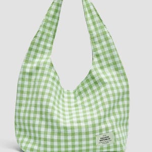 May include: A light green and white gingham patterned hobo bag with a single shoulder strap. A small rectangular fabric label is stitched to the lower right corner, featuring the text PACIFIC REPUBLIC along with smaller printed details.