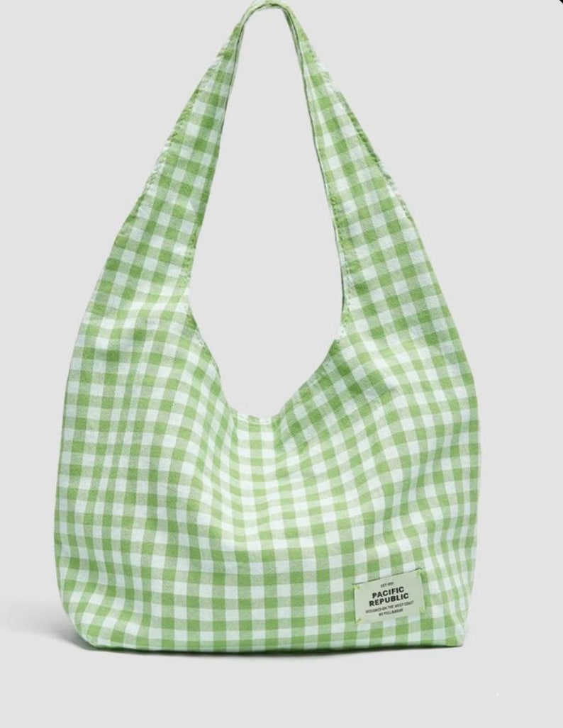 May include: A light green and white gingham patterned hobo bag with a single shoulder strap. A small rectangular fabric label is stitched to the lower right corner, featuring the text PACIFIC REPUBLIC along with smaller printed details.