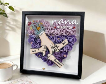 Caja de sombra personalizada con forma de corazón y rosa, marco con nombres de niños y manos sosteniendo un objeto, regalo para el Día de la Madre.