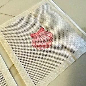 May include: Square, off-white needlepoint canvas with a red seashell design. The seashell is hand-stitched with a detailed outline and shading, creating a three-dimensional effect. The canvas has a grid-like pattern and a finished edge.