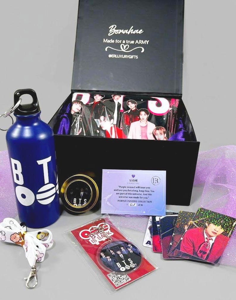 May include: A gift box with various BTS-themed merchandise. Includes a blue water bottle with white lettering, a keychain, a pin, photo cards, and a box with images of the band members. The box has the text "Borahae" and "Made for a true ARMY".