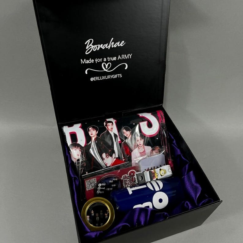 May include: A black gift box lined with purple satin containing BTS merchandise. The lid interior features the text Borahae, Made for a true ARMY, and @ERLUXURYGIFTS. Inside are photo cards, a blue tumbler, and a small circular gold-rimmed item.