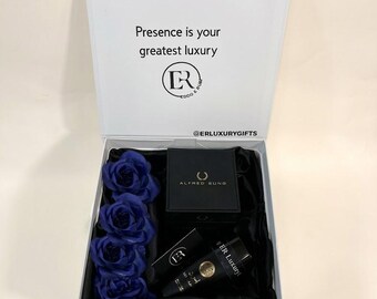 May include: A white gift box with a hinged lid containing four deep blue artificial roses, a black Alfred Sung box, and a black ER Luxury tube. The inside lid features the text "Presence is your greatest luxury" and "@ERLUXURYGIFTS".