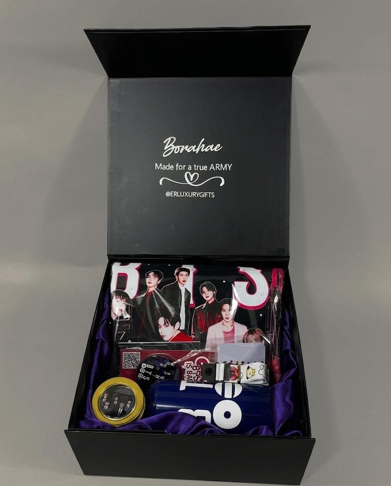 May include: A black gift box with a purple satin lining containing BTS merchandise. The lid interior features the text "Borahae Made for a true ARMY @ERLUXURYGIFTS". Items include a photo-printed pouch, a round tin, and a blue water bottle.