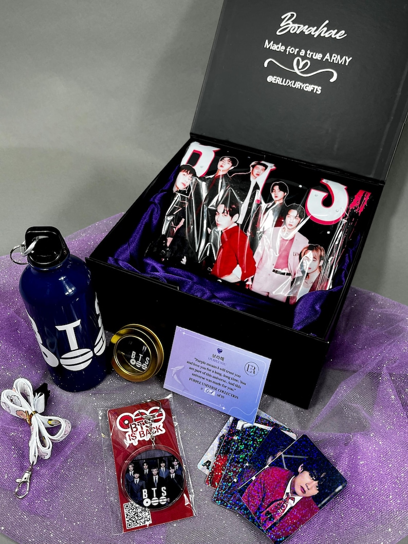 May include: A black gift box containing a BTS-themed collection, including a blue water bottle with white text, a round metal tin, a white lanyard, a circular keychain with a group photo, a purple information card, and several holographic photo cards.