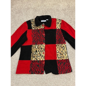 May include: A long-sleeved button-down shirt featuring a patchwork design of solid black, solid red, and animal print panels. The shirt has a black collar, red buttons, and a label at the neckline that reads BEA. The sleeves are solid black and red.