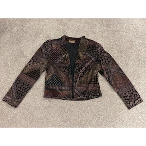 May include: A long-sleeved blazer featuring a dark, multi-colored patchwork pattern with shades of brown, black, and deep purple. The garment has a notched lapel, a single front hook-and-eye closure, and a black interior lining with a Gregg label.