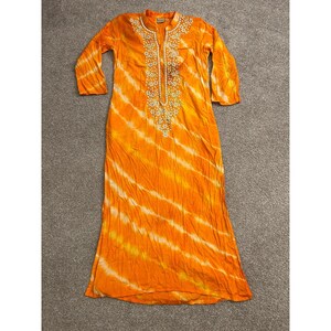 Könnte beinhalten: Ein langärmeliges orangefarbenes Kleid mit einem diagonalen Batikmuster in Gelb- und Weißtönen. Das Kleidungsstück hat einen geschlitzten Ausschnitt, der mit weißer Blumenstickerei und kleinen runden Verzierungen in der Mitte verziert ist.