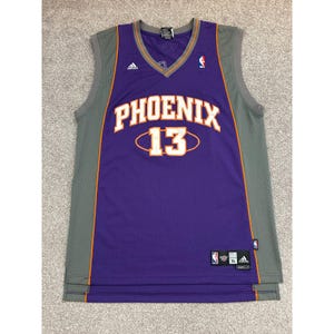 Op de afbeelding: Een paars en grijs mouwloos basketbalshirt met het woord PHOENIX in witte letters met oranje rand boven het nummer 13 in een wit ovaal. Het shirt bevat een Adidas-logo, een NBA-logo en een XL-maatlabel aan de onderkant van de voorzijde.