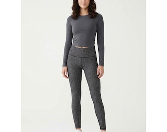 May include: A charcoal gray long-sleeve crew neck top paired with high-waisted black and white speckled leggings. The outfit is completed with a pair of plain white athletic sneakers, creating a coordinated set of activewear clothing.