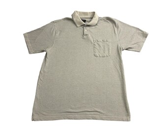 Könnte beinhalten: Ein kurzärmeliges Poloshirt mit einer hellen Grundfarbe und einem dichten, kleinteiligen dunklen Gittermuster. Das Kleidungsstück verfügt über einen einfarbigen hellen Kragen, eine Knopfleiste mit drei Knöpfen und eine Brusttasche links.