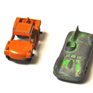 May include: Two vintage toy cars, one orange and one black with green accents. The orange car is a jeep-like vehicle with a removable top. The black car is a race car with a spoiler.