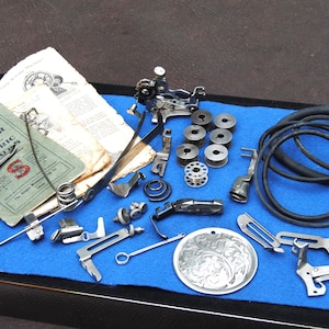May include: A collection of vintage Singer sewing machine parts and accessories, including bobbins, presser feet, and instruction manuals. The items are arranged on a blue felt surface.