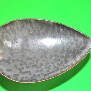 Può includere: Un cucchiaio vintage in metallo con finitura smaltata grigia. Il cucchiaio ha una ciotola arrotondata e un manico lungo.