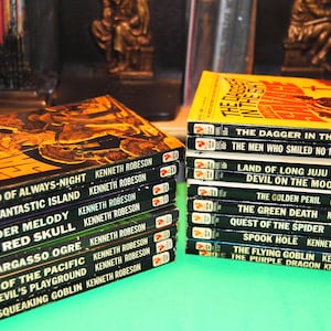 Puede incluir: Una pila de libros de bolsillo con cubiertas negras y amarillas. Los libros se titulan "Land of Always-Night", "The Fantastic Island", "Murder Melody", "The Red Skull", "The Sargasso Ogre", "Pirate of the Pacific", "The Devil's Playground", "The Squeaking Goblin", "The Dagger in the Sky", "The Men Who Smiled No More", "Land of Long Juju", "Devil on the Moon", "The Golden Peril", "The Green Death", "Quest of the Spider", "Spook Hole", "The Flying Goblin" y "The Purple Dragon". Todos los libros son de Kenneth Robeson.