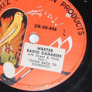 Può includere: Primo piano di un'etichetta di un disco in vinile vintage. L'etichetta arancione presenta un'illustrazione di canarino giallo, note musicali e il testo "MASTER RADIO CANARIES" e "COME BACK TO SORRENTO". Il disco è nero.
