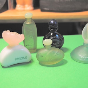 May include: A selection of miniature perfume bottles in different shapes and colours. The bottles include a white one with a pink flower-shaped top, a green bottle with leaf details, and a black bottle with the text "NUIT ORCHID".