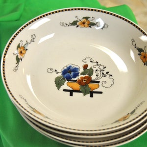 May include: A set of four white ceramic bowls with a black and gold rim. The bowls feature a floral design with blue, orange, and yellow flowers.