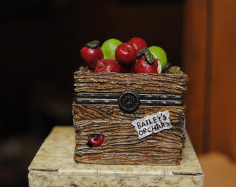 May include: A decorative wooden box filled with red and green apples. The box has a rustic, textured appearance with a metal clasp and the text "Bailey's Orchard" on a small tag.