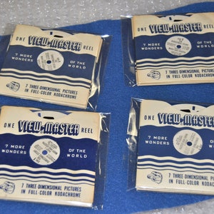 Könnte beinhalten: Vier View-Master-Rollen, jede in einer durchsichtigen Plastikhülle. Die Rollen sind weiß mit blau-weißen Streifen und tragen den Text "ONE VIEW-MASTER REEL", "7 MORE WONDERS", "OF THE WORLD" und "7 THREE-DIMENSIONAL PICTURES IN FULL-COLOR KODACHROME".