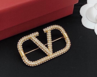 Broche de cristal con la firma VLogo en metal dorado (sin caja)