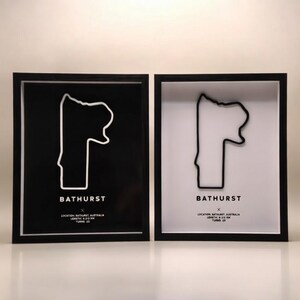 May include: Two framed artworks featuring a minimalist outline of a race track. One has a black background with a white track outline, the other has a white background with a black track outline. The word "BATHURST" is printed below the track outline.