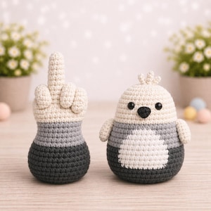 May include: Two handmade crochet figures: a hand with the middle finger raised and a bird-like creature. The hand is beige, gray, and black. The bird is white, gray, and black with small wings and a black beak.