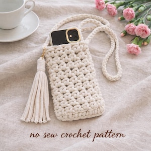May include: Cream-colored crochet phone case with a long strap and a tassel. The phone case is made of a thick, woven material and has a gold-colored clasp. The text "no sew crochet pattern" is at the bottom of the image.