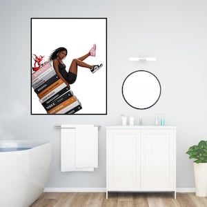 May include: A framed art print featuring a fashion illustration of a person in a black dress and sneakers, sitting atop a stack of books. The books have titles like "Vogue" and "Louis Vuitton". A splash of red is visible on the left.
