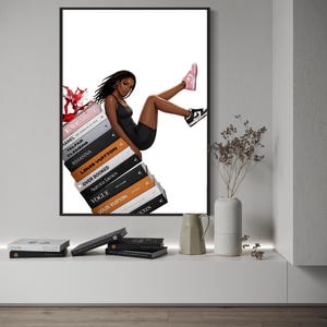 May include: A framed art print featuring a stylish illustration of a person in a black outfit, seated atop a stack of fashion books. The books include titles like "Dior" and "Louis Vuitton." The person is wearing pink and black sneakers.