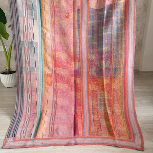 Puede incluir: Una manta rectangular con diseño de patchwork que presenta paneles verticales en tonos rosa, naranja, azul y blanco. La tela muestra intrincados patrones de costura continua, con motivos de cachemira y bordes a rayas visibles.