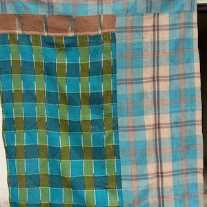 May include: A patchwork quilt with a plaid pattern in shades of blue, green, and tan. The quilt is made of multiple squares of fabric sewn together. The design is a classic plaid, with intersecting lines creating a grid-like pattern.