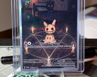 May include: A Mimikyu Pokémon trading card in a protective case. The card features a detailed illustration of Mimikyu in a dark, gothic setting with the text "Cursed Playtime". The card is held by a clear plastic stand.