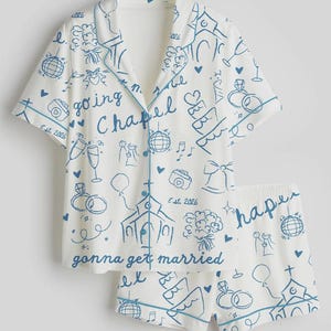 May include: White pajama set with a blue wedding-themed doodle print. The short-sleeved top and shorts feature drawings of wedding rings, churches, and the text "going Chapel" and "gonna get married".