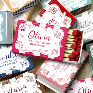 May include: A collection of personalized matchboxes in various colors, including pink, blue, and green. Each box features a name and the text "Will you be my bridesmaid?" or "Will you be my man of honor?" with decorative elements.