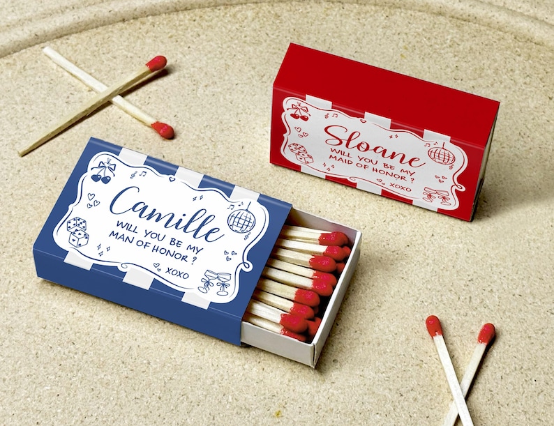 May include: Two matchboxes, one blue and one red, with white decorative text. The blue box says "Camille, will you be my man of honor? xoxo." The red box says "Sloane, will you be my maid of honor? xoxo."