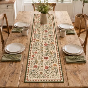 May include: A long rectangular table runner featuring a cream-coloured background with a dense, colourful botanical print of various wildflowers in shades of red, orange, yellow, and green, bordered by a dark green and white triangular pattern.