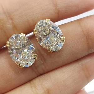 May include: A pair of oval-cut diamond stud earrings. The diamonds are set in a gold prong setting. The earrings are displayed against a neutral background.