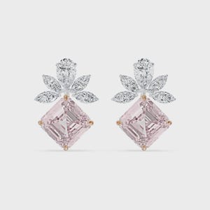 May include: A pair of elegant earrings featuring a light pink, square-cut gemstone at the base. Above the pink stone is a cluster of smaller, clear gemstones arranged in a floral pattern. The earrings have a gold-colored setting.